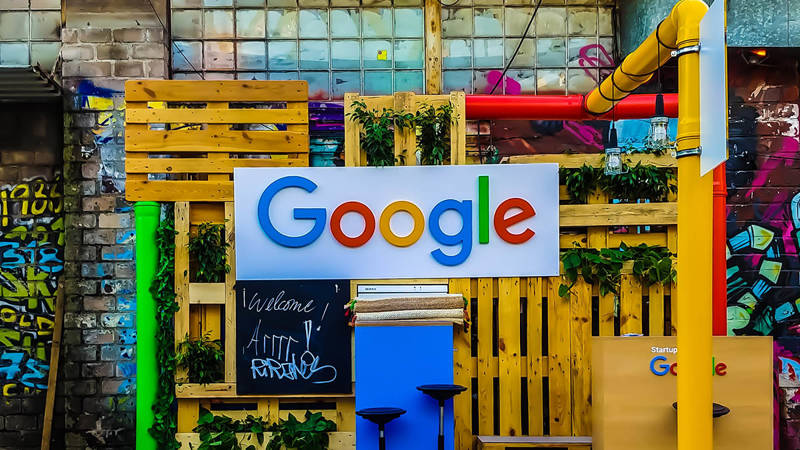 A sign with the 'Google' logo on it in front of brightly covered wood and pipes