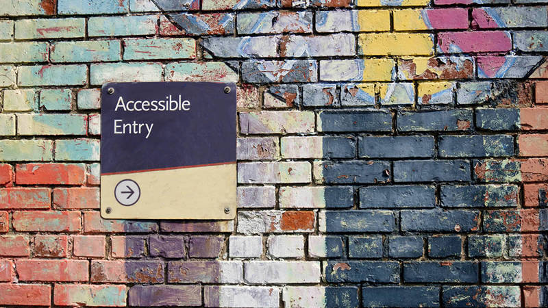 Brick wall with a sign on it that says 'Accessible entry' with an arrow below it