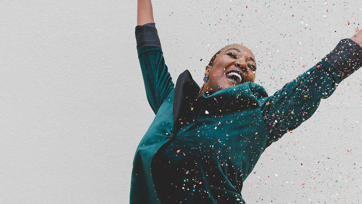 A woman throwing up her arms in celebration surrounded by confetti