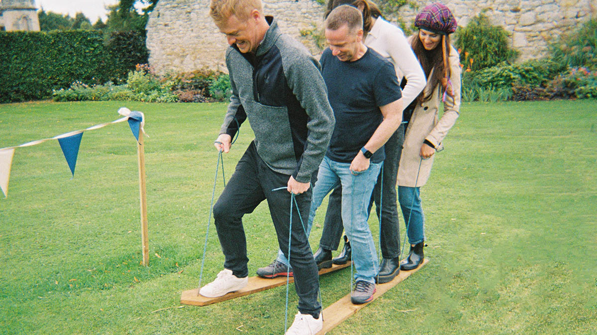 Four people trying to walk along with two planks attached to their feet
